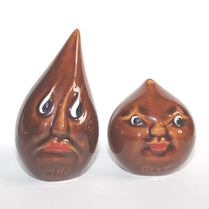 May include: A pair of brown ceramic salt and pepper shakers with facial features. One is teardrop-shaped and labeled "DRIP", the other is round and labeled "DASH". Both have white eyes and red lips.