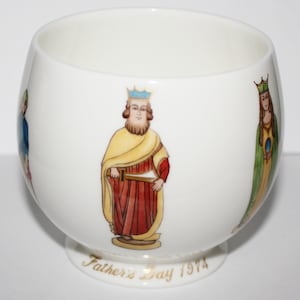 Könnte beinhalten: Weiße Keramikschale mit goldfarbenem Rand und einer goldenen Inschrift mit der Aufschrift "Father's Day 1974". Die Schale zeigt ein handgemaltes Design mit vier Figuren in mittelalterlicher Kleidung, darunter ein König, eine Königin und zwei weitere Figuren.