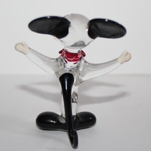 May include: A glass figurine of a dog with black ears, a red bow tie, and black legs. The dog is standing on its hind legs with its front legs outstretched.