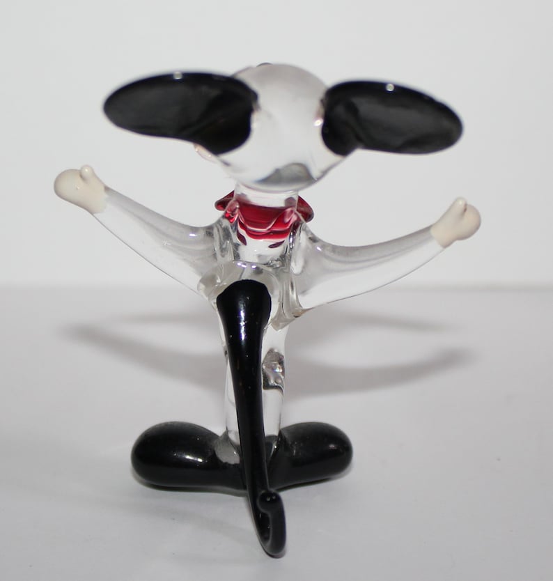 May include: A glass figurine of a dog with black ears, a red bow tie, and black legs. The dog is standing on its hind legs with its front legs outstretched.
