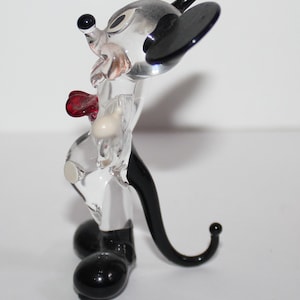 May include: A clear glass figurine of Mickey Mouse. The figurine is standing with its arms at its sides. Mickey is wearing a red bow tie and has black ears and shoes.