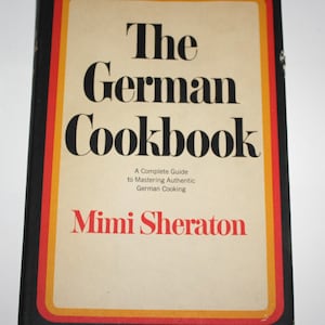 May include: The German Cookbook by Mimi Sheraton, a complete guide to mastering authentic German cooking. The book cover features a black background with a yellow, orange, and red border.