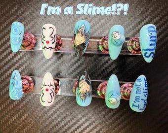 May include: A set of ten artificial nails with various designs. The nails feature cartoon characters, text that reads "Slurp" and "I'm not a bad slime", and other abstract designs. The nails are in shades of blue, white, and black.