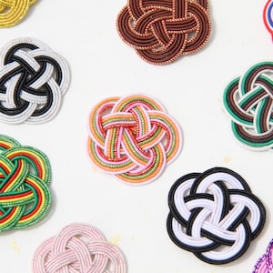 May include: A selection of colourful Japanese Mizuhiki knots. The image shows various woven designs in shades of red, green, white, black, and gold. These decorative knots are often used for gift wrapping and special occasions in Japan.