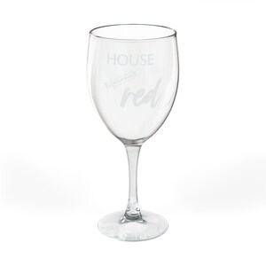 Może przedstawiać: Przezroczysty kieliszek do wina ze stopką i okrągłą podstawą. Na szkle wygrawerowano słowa "HOUSE red". Mała grafika korkociągu jest wygrawerowana między słowami "HOUSE" i "red".