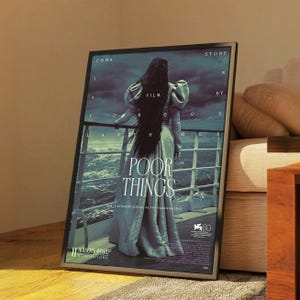 May include: Framed movie poster for "Poor Things" featuring Emma Stone. The poster has a dark, moody aesthetic with a woman in a long dress on a ship. The poster includes the film title, credits, and Academy Award nominations.