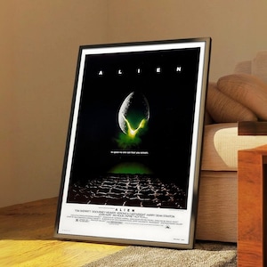 Könnte beinhalten: Gerahmtes Filmplakat für den Film "Alien". Das Poster zeigt den Filmtitel oben, mit einem Bild eines Alien-Eies, das grünes Licht aussendet. Der untere Teil des Posters enthält den Abspann des Films.