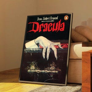 Könnte beinhalten: Ein gerahmtes rechteckiges Poster mit dem Titel Dracula in großen roten Buchstaben und dem Text Bram Stoker's Original darüber. Das Bild zeigt eine blasse Hand mit langen Fingernägeln, die auf dem Rand eines dunklen Sarges mit Metallbeschlägen ruht.