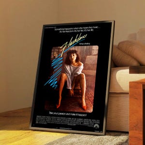 May include: Framed movie poster for the film "Flashdance." The poster features a woman in a gray sweater and red heels. Text includes the film title, "What a feeling," and the tagline "Take your passion and make it happen!"