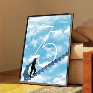 Pode incluir: Pôster emoldurado com uma imagem surreal de uma pessoa subindo uma escada em direção a um céu nublado. O número 75 é proeminente, com texto indicando o Festival de Cinema de Cannes, 17-28 de maio de 2022.