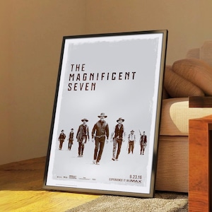 以下が含まれることがあります： 映画「The Magnificent Seven」の額入りポスター。カウボーイ姿の男性たちが観客に向かって歩いている。ポスターは薄いグレーの背景に、映画のタイトルが大きな濃い色の文字で書かれている。公開日は9.23.16。
