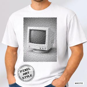 May include: A white short-sleeved t-shirt featuring a black and white pixel art graphic of a vintage computer monitor. The design is rendered in a stippled dot pattern. A circular badge on the lower left displays the text PIXEL ART STYLE.