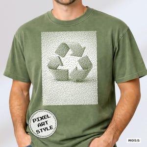 May include: Moss green t-shirt featuring a pixel art style recycle symbol. The graphic is a dotted design in shades of green and white. The shirt has a crew neck and short sleeves. The words "Pixel Art Style" are in a circular logo on the bottom left.