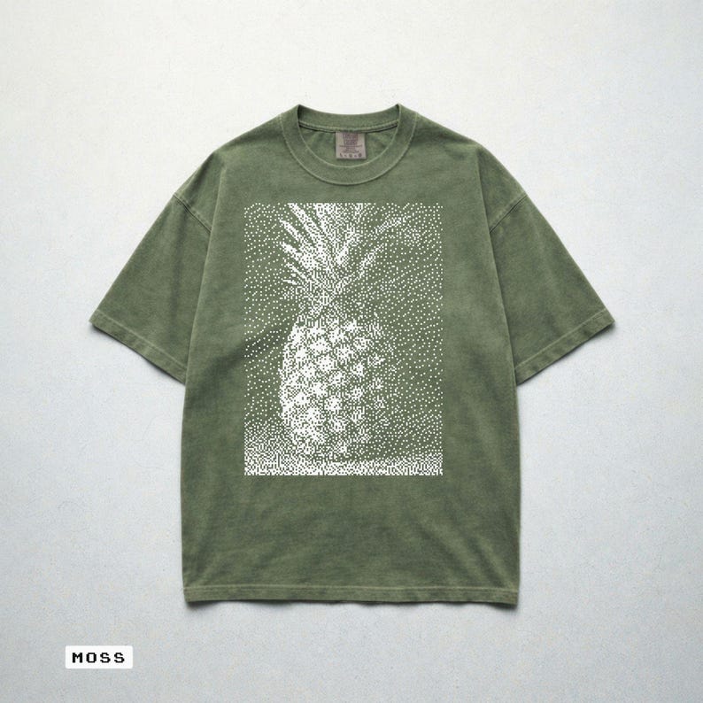 May include: Moss green t-shirt featuring a white dotted pineapple design. The short-sleeved shirt has a relaxed fit and a crew neck. The word "MOSS" is printed at the bottom of the image.