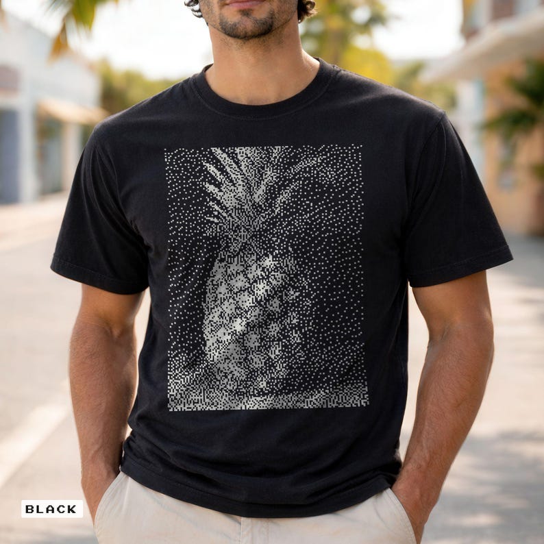 May include: Black t-shirt featuring a detailed, pixelated pineapple design in shades of white and gray. The shirt has a classic crew neck and short sleeves. The word "BLACK" is printed at the bottom left corner of the shirt.