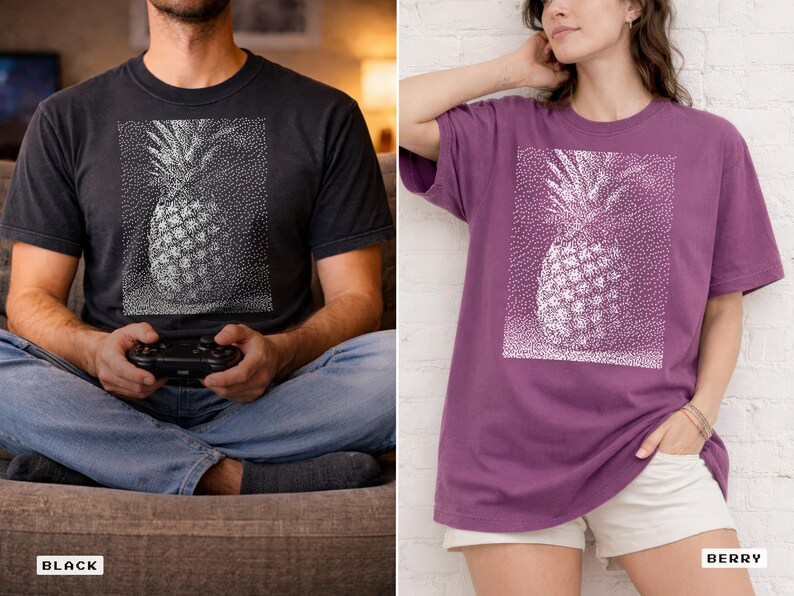 May include: Black and berry-colored t-shirts featuring a white dotted pineapple design. The shirts are short-sleeved and have a relaxed fit. The black shirt is worn by a person holding a game controller. The berry shirt is worn by a person with their hand in their pocket.