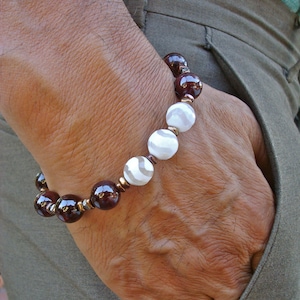 Puede incluir: Un brazalete hecho de cuentas de ágata roja oscura y blanca con separadores de cobre.