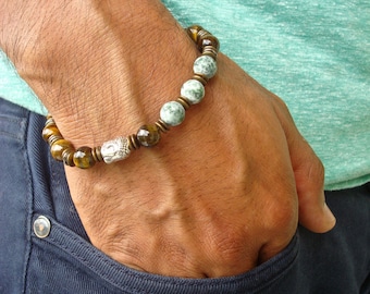 May include: A brown and green beaded bracelet with a silver charm. The bracelet is worn on a person's wrist.
