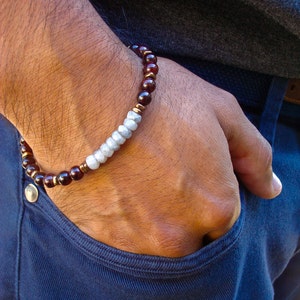 Puede incluir: Un brazalete con cuentas de color rojo oscuro y plata. El brazalete se lleva en la muñeca.