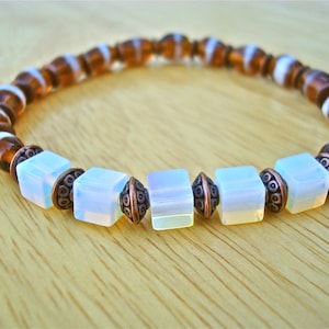 May include: A brown and white beaded bracelet with copper accents and iridescent white square beads.