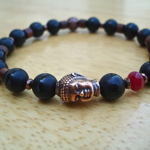 May include: A black onyx beaded bracelet with copper spacers and a copper Buddha head charm. A single red gemstone bead is included in the bracelet.
