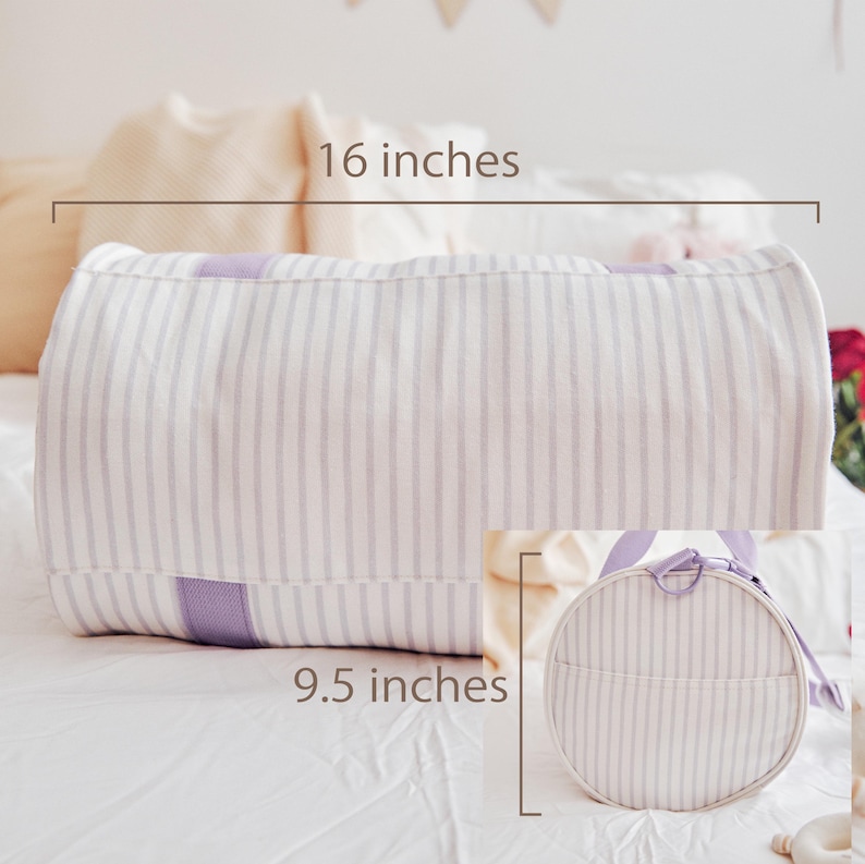 May include: A white and lavender striped bolster pillow, 16 inches long, with a matching round bag, 9.5 inches in diameter. The pillow and bag feature a soft, vertical stripe pattern and are made of a light-colored fabric. The bag has a lavender handle.