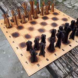 Puede incluir: Un juego de ajedrez de madera con un tablero marrón claro y cuadrados marrones oscuros. Las piezas de ajedrez están cortadas con láser, con piezas marrones claras y oscuras dispuestas en el tablero. El tablero tiene números y letras en los bordes.