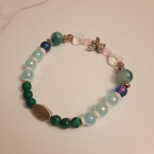 Puede incluir: Una pulsera de cuentas con cuentas verdes, azules y rosas. Incluye un dije de &aacute;ngel plateado y un dije ovalado de metal con la palabra "Loved". Las cuentas var&iacute;an en tama&ntilde;o y textura.