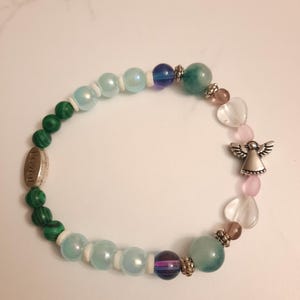 Puede incluir: Una pulsera de cuentas con cuentas verdes de malaquita, azules iridiscentes y rosas en forma de coraz&oacute;n. Tambi&eacute;n hay un dije de &aacute;ngel plateado y un dije plateado con la palabra "Loved".