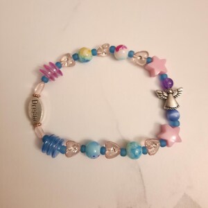 May include: A beaded bracelet featuring a variety of colorful beads, including pink stars, clear hearts, and blue and multicolored round beads. A silver charm with the word "Dream" and an angel charm are also included.