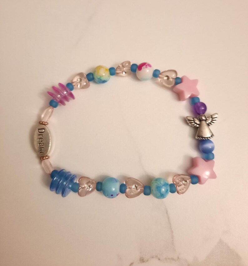 May include: A beaded bracelet featuring a variety of colorful beads, including pink stars, clear hearts, and blue and multicolored round beads. A silver charm with the word "Dream" and an angel charm are also included.