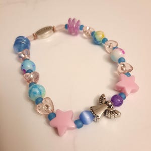 May include: A beaded bracelet featuring a mix of colorful beads. The bracelet includes blue, pink, and purple beads, along with star and heart-shaped accents. A silver angel charm adds a decorative touch to this handmade jewelry.