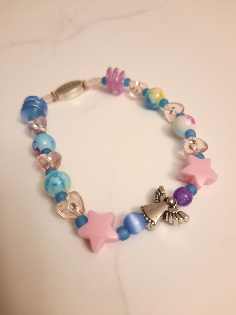 May include: A beaded bracelet featuring a mix of colorful beads. The bracelet includes blue, pink, and purple beads, along with star and heart-shaped accents. A silver angel charm adds a decorative touch to this handmade jewelry.