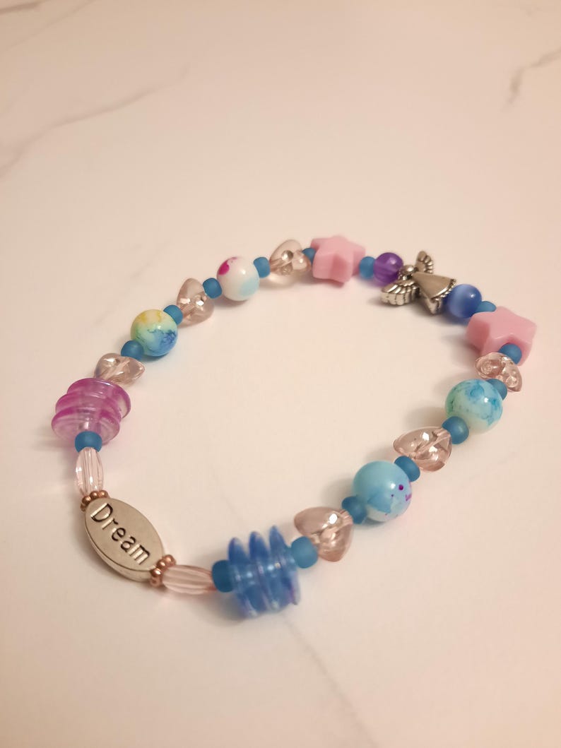 May include: A beaded bracelet with a variety of colorful beads. The bracelet features pink star-shaped beads, blue and purple beads, and a silver charm with the word "Dream". The bracelet is approximately 7 inches in length.