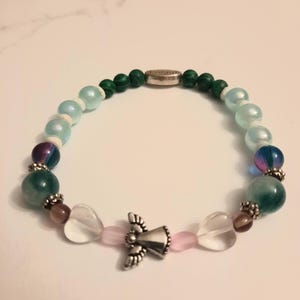 Puede incluir: Una pulsera de cuentas con un dije de &aacute;ngel plateado, cuentas claras en forma de coraz&oacute;n y varias cuentas de colores. La pulsera incluye cuentas verdes, azules, moradas y rosas, con un cierre plateado.