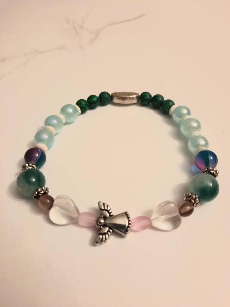 Puede incluir: Una pulsera de cuentas con un dije de &aacute;ngel plateado, cuentas claras en forma de coraz&oacute;n y varias cuentas de colores. La pulsera incluye cuentas verdes, azules, moradas y rosas, con un cierre plateado.