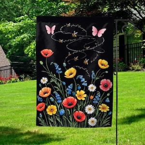 May include: Black garden flag featuring colorful flowers, butterflies, and bees. The flag has the words "fuck trump" written on it. The flowers include red poppies, yellow daisies, and bluebells. The butterflies are pink.
