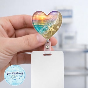 May include: Heart-shaped badge reel featuring a beach scene with a sunset, waves, and a starfish. The reel has a clear plastic body and a blank white ID card holder. The words "Personalized Gift" are in a blue circle.