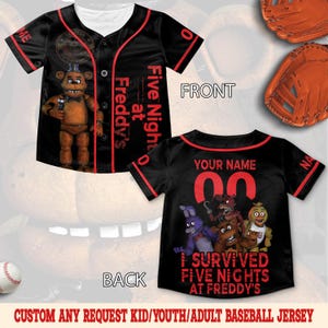 May include: Black baseball jersey with red trim and text "Five Nights at Freddy's". The front features a character graphic. The back has a customizable name and number, with the text "I Survived Five Nights at Freddy's".