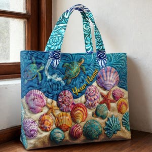 May include: A quilted tote bag featuring a beach scene with seashells, starfish, and sea turtles. The bag has a blue background with a sandy foreground and a handle with a blue and white swirl pattern. The text "Your Name" is visible on the bag.