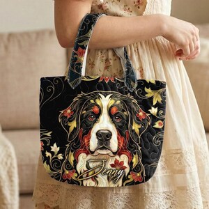 Può includere: Borsa tote nera con un design di cane da montagna bernese e accenti floreali rossi, gialli e bianchi. La borsa ha una texture trapuntata e un manico con un motivo floreale. Il nome "Jenny" è scritto sulla borsa.