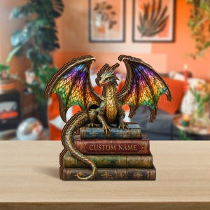 May include: A dragon figurine with iridescent, stained-glass style wings in shades of purple, green, and orange, perched atop a stack of four vintage-style books. The second book from the top features the text CUSTOM NAME in gold lettering.