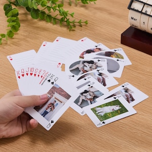 Op de afbeelding: Een set gepersonaliseerde speelkaarten met eigen foto's op de voorzijde, waaronder afbeeldingen van een persoon en honden. De kaarten tonen standaard kleursymbolen en rangen in rode en zwarte inkt, met enkele kaarten voorzien van lijnen.
