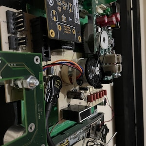 Op de afbeelding: Close-up van elektronische printplaten met diverse componenten, waaronder condensatoren, weerstanden en geïntegreerde circuits. De platen zijn groen en zwart, met rode en gouden componenten. De afbeelding toont een complexe opstelling van draden en connectoren.