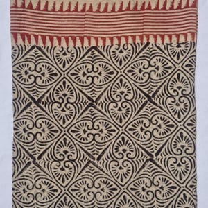 May include: A textile with a cream-colored background and a repeating pattern of dark brown floral shapes. The top border features a red striped design. The fabric is likely cotton or linen, suitable for home decor or apparel.