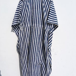 May include: A navy blue and white striped caftan dress hanging on a wooden hanger. The dress has a loose, flowing design with vertical stripes. The fabric appears to be lightweight, suitable for warm weather.