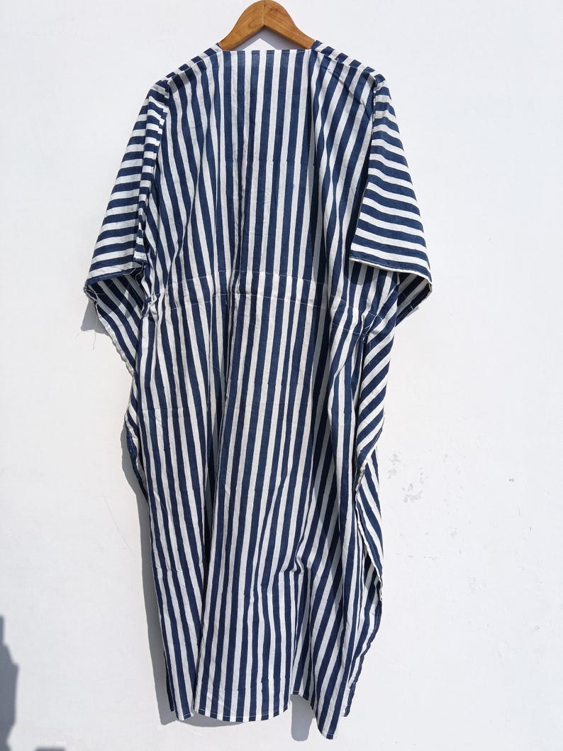 May include: A navy blue and white striped caftan dress hanging on a wooden hanger. The dress has a loose, flowing design with vertical stripes. The fabric appears to be lightweight, suitable for warm weather.
