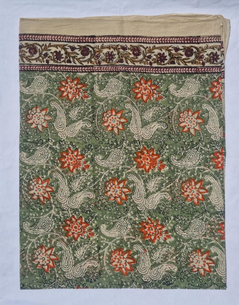 May include: A green textile with a floral and paisley pattern. The design features orange flowers and off-white paisley shapes on a green background. A border with floral and leaf patterns in burgundy and brown accents the top edge.