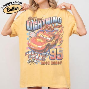 Puede incluir: Una camiseta amarilla con un dise&ntilde;o de Rayo McQueen de la pel&iacute;cula Cars. El dise&ntilde;o incluye el texto "Street Legend Lightning McQueen", "Need for Speed" y el n&uacute;mero "95". La camiseta est&aacute; etiquetada como "Comfort Colors Butter".