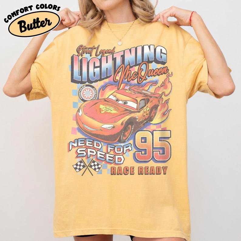 Puede incluir: Una camiseta amarilla con un dise&ntilde;o de Rayo McQueen de la pel&iacute;cula Cars. El dise&ntilde;o incluye el texto "Street Legend Lightning McQueen", "Need for Speed" y el n&uacute;mero "95". La camiseta est&aacute; etiquetada como "Comfort Colors Butter".